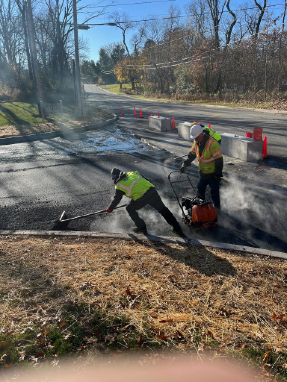Beckage crew raking and compacting hot asphalt at a commercial road entrance in NJ