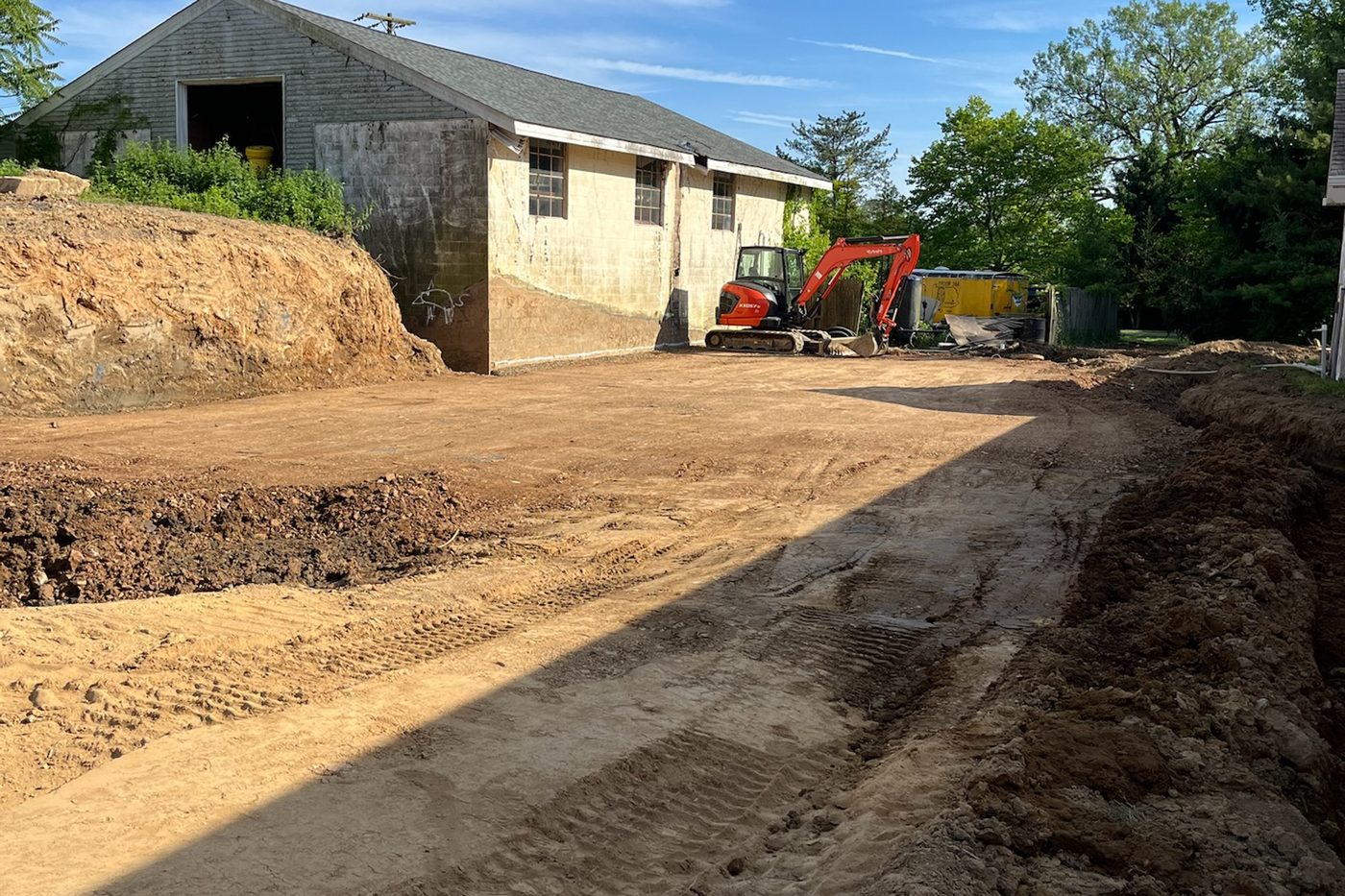 Graded and leveled dirt pad with a mini excavator on site, prepped for paving by Beckage in NJ
