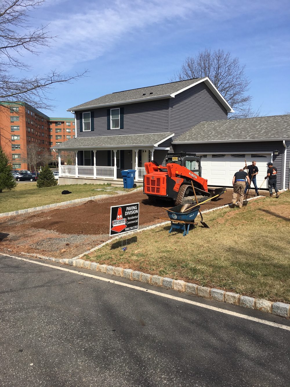 Beckage crew grading the stone base for a new residential driveway with a Beckage Paving Division sign in NJ