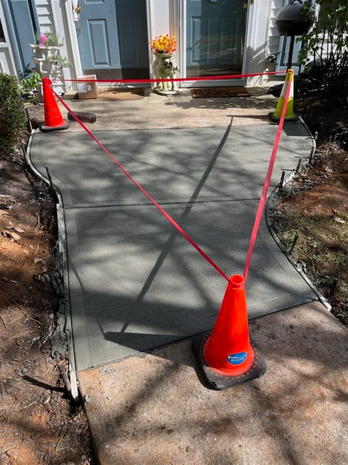 Freshly poured concrete residential walkway by Beckage Sealcoating, cordoned off with orange safety cones and red barrier tape while curing