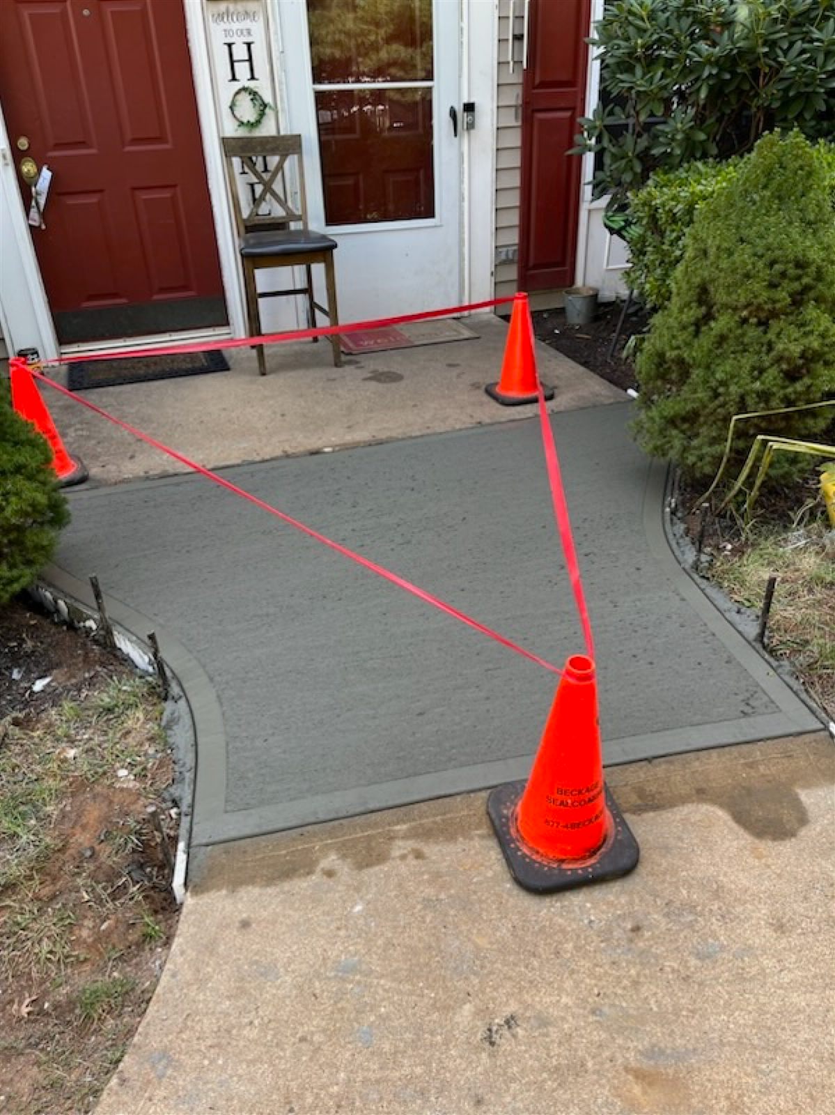 New concrete front walkway poured by Beckage, roped off with branded Beckage safety cones during curing