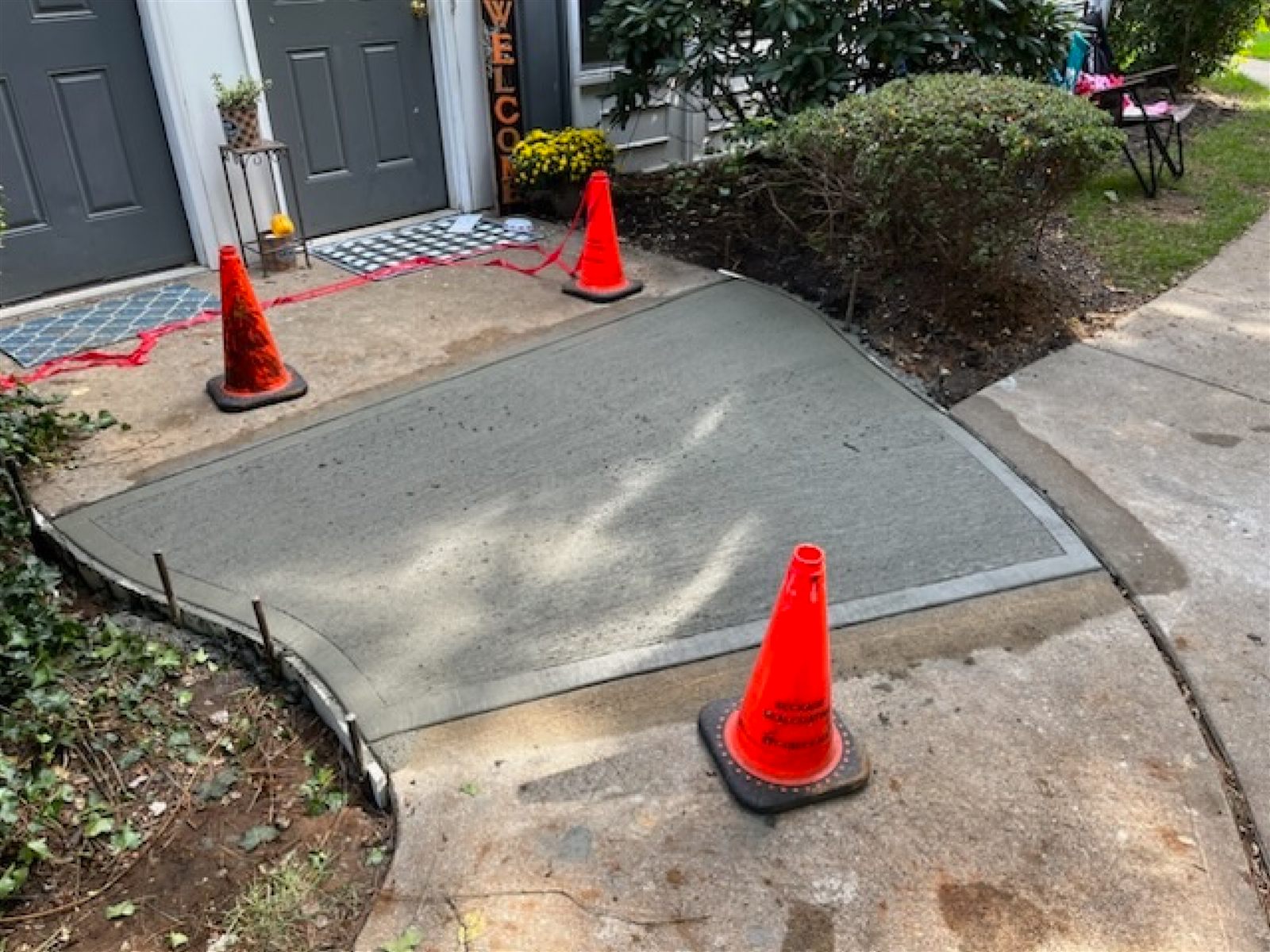 Newly installed concrete sidewalk section and ramp transition by Beckage Sealcoating, marked off with cones