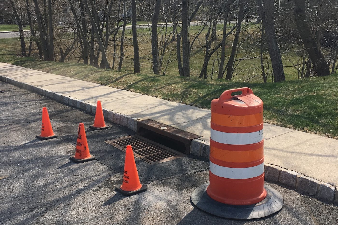 Finished storm drain grate reset flush in the curb with fresh asphalt, cordoned off with Beckage cones in NJ
