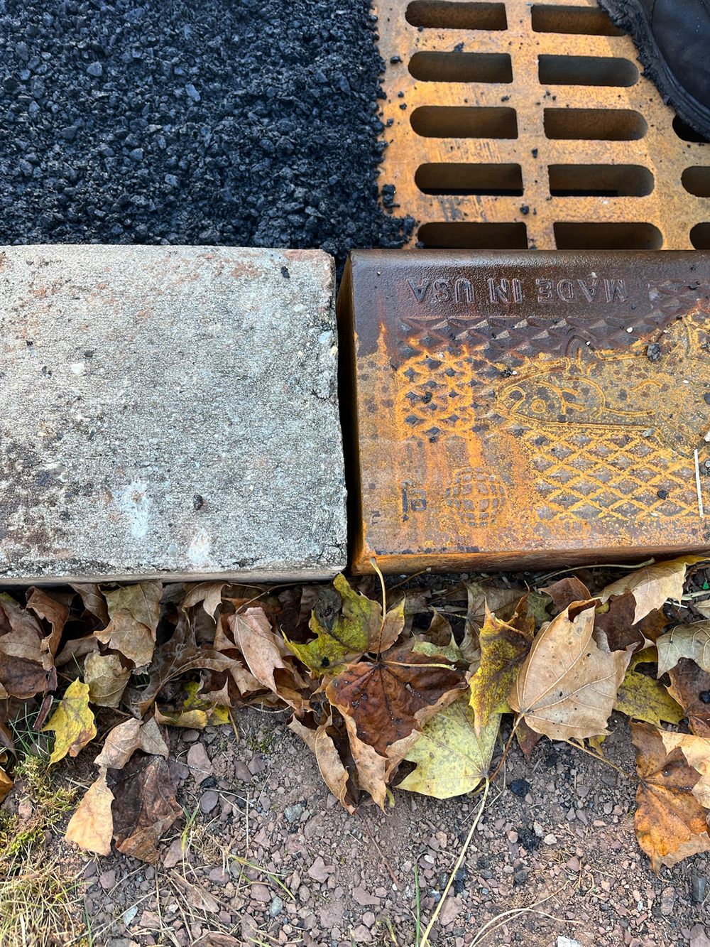 Close-up of a cast-iron catch basin frame set flush against the concrete curb and fresh asphalt along a new curb line in New Jersey